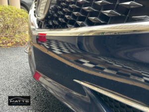 A technician using a rotary polisher to perform a paint correction on the side panel of a dark vehicle.
