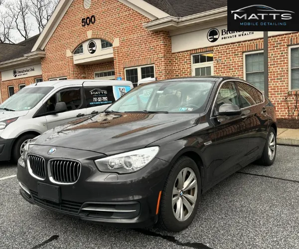 clean, dark grey BMW sedan parked in a parking lot in front of a brick building.