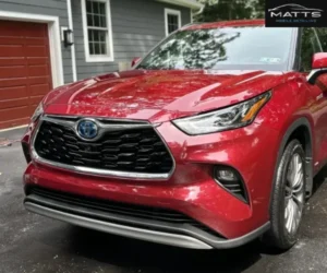 A close-up front view highlighting the front grille and hood of a glossy red Toyota Highlander Hybrid