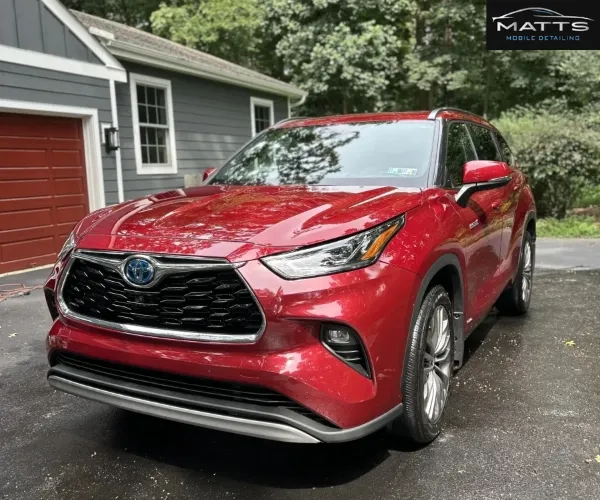A glossy red Toyota Highlander Hybrid SUV parked in a residential driveway in front of a grey garage