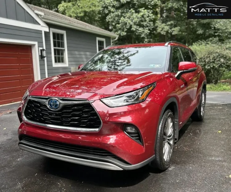 Front three-quarter view of a glossy red SUV parked on a driveway in front of a house.